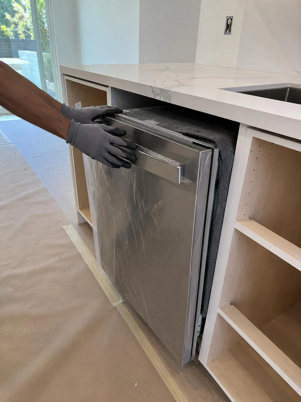 Technician repairing stainless dishwasher under counter in San Diego home