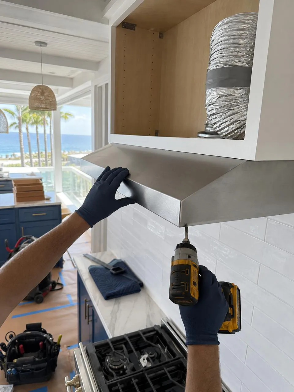 Technician mounting stainless range hood above a gas cooktop