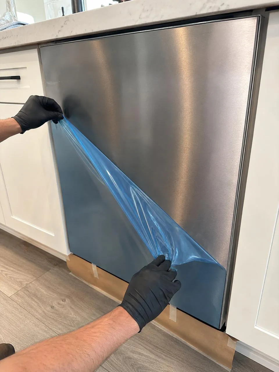 Technician peeling protective film from a new stainless dishwasher panel