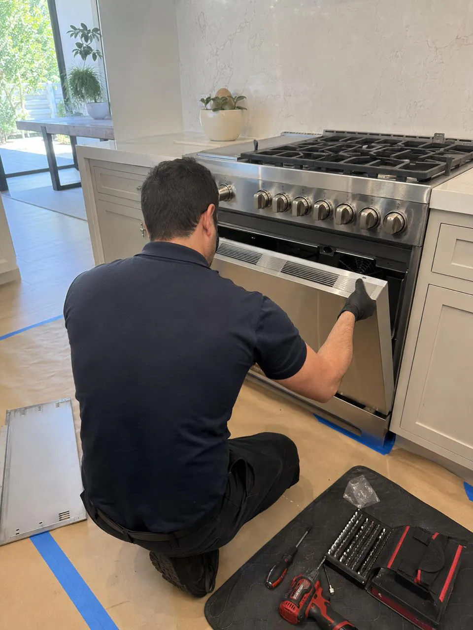 Technician servicing stainless gas range oven door in San Diego kitchen