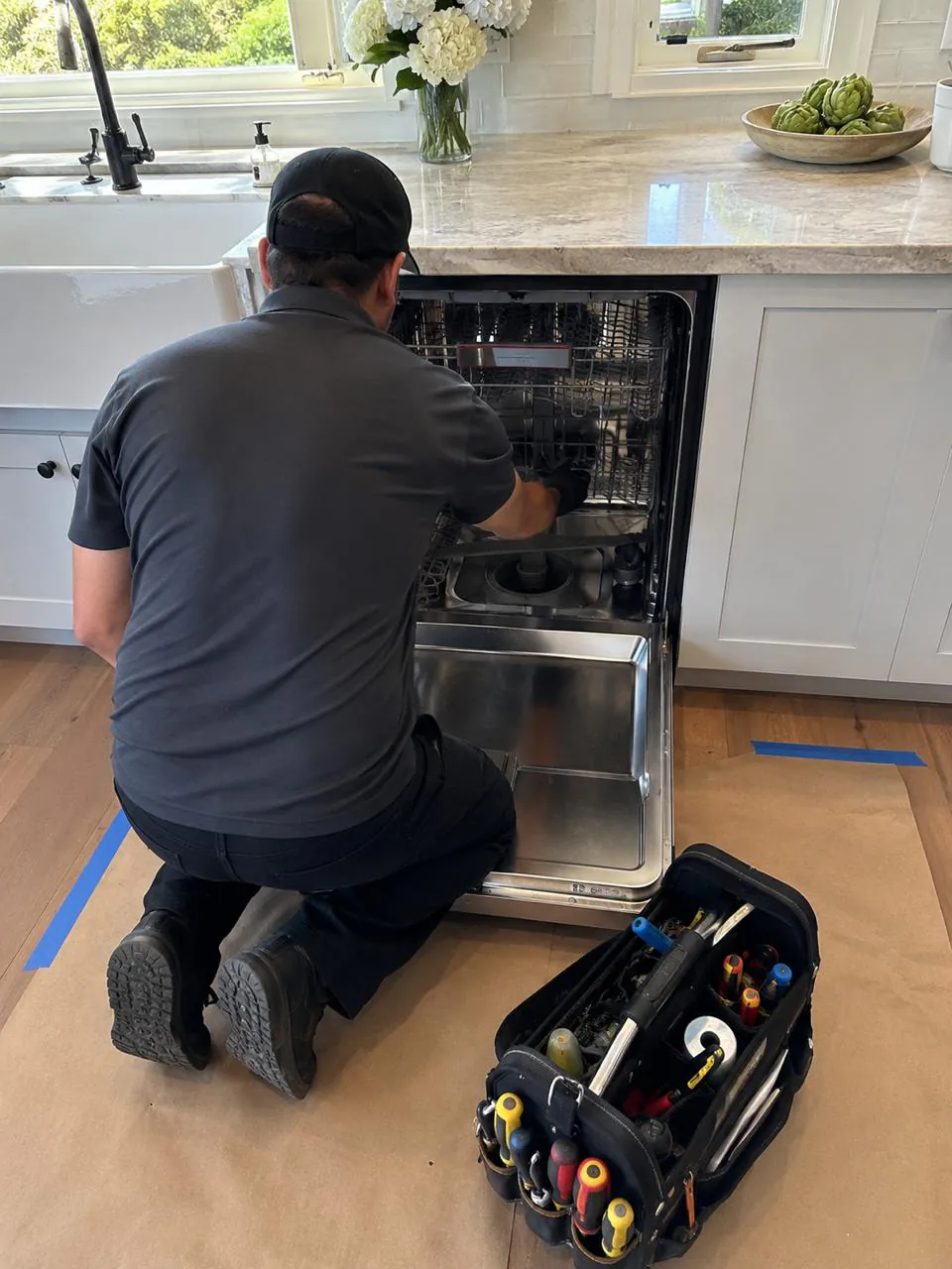 Technician repairing built-in dishwasher in a bright Southern California kitchen