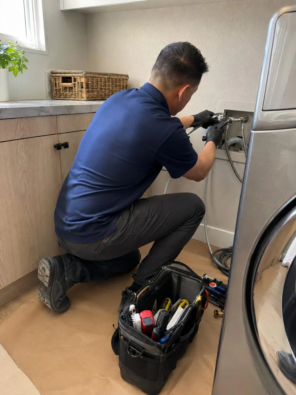 Technician connecting washer water supply hoses in a laundry room