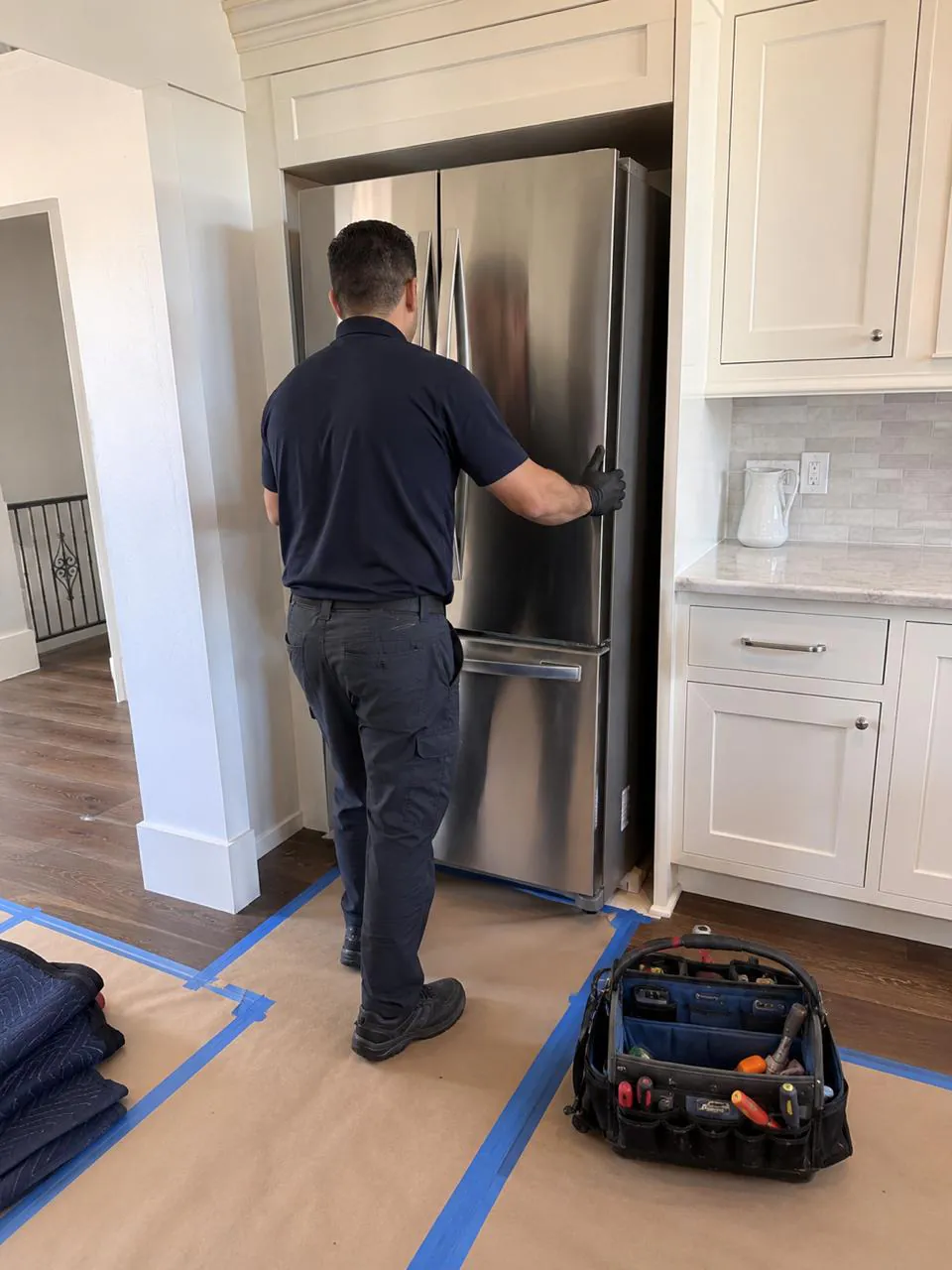 Technician adjusting stainless steel refrigerator in San Diego home kitchen