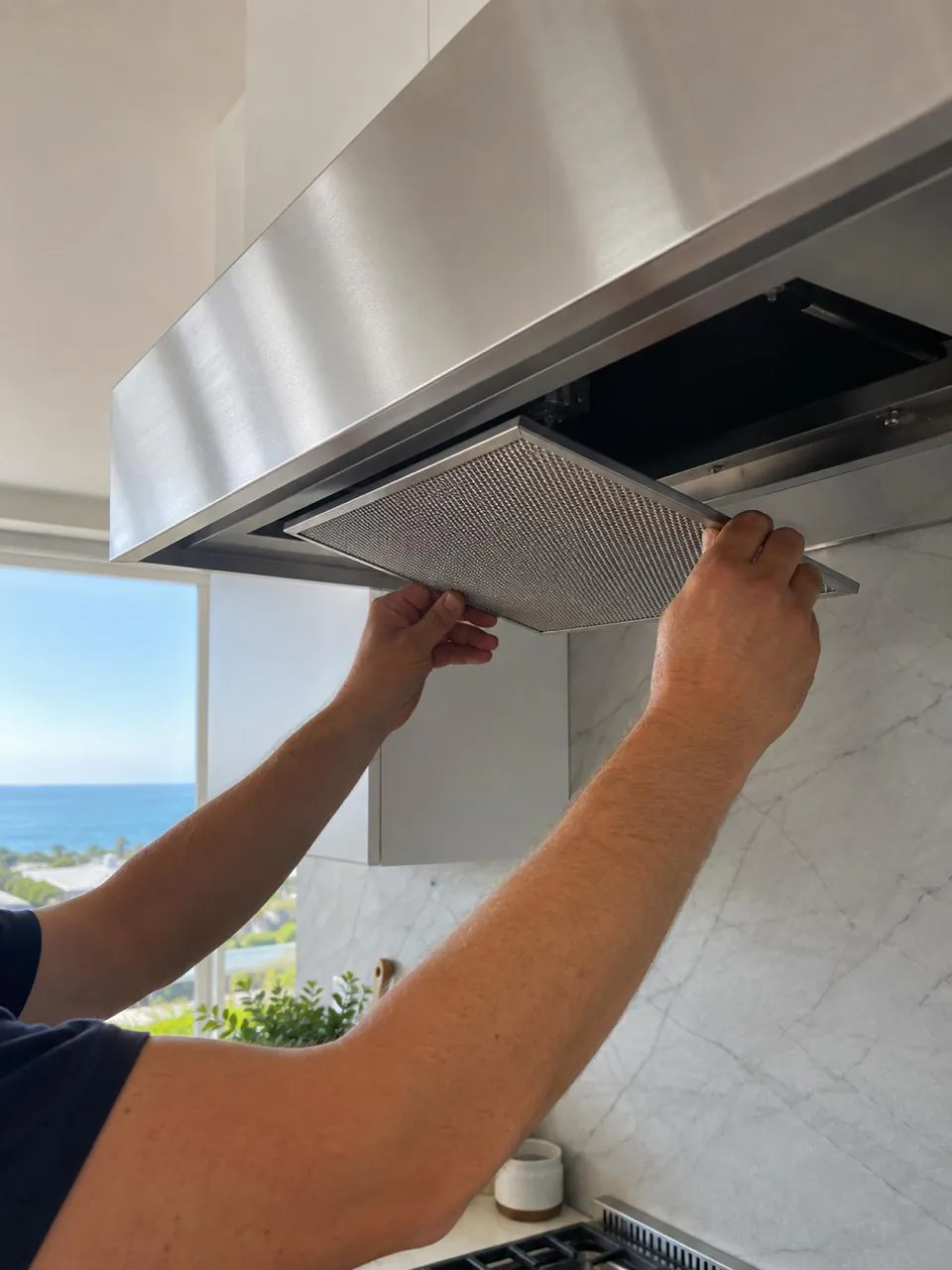 Technician removing range hood grease filter in an oceanview kitchen